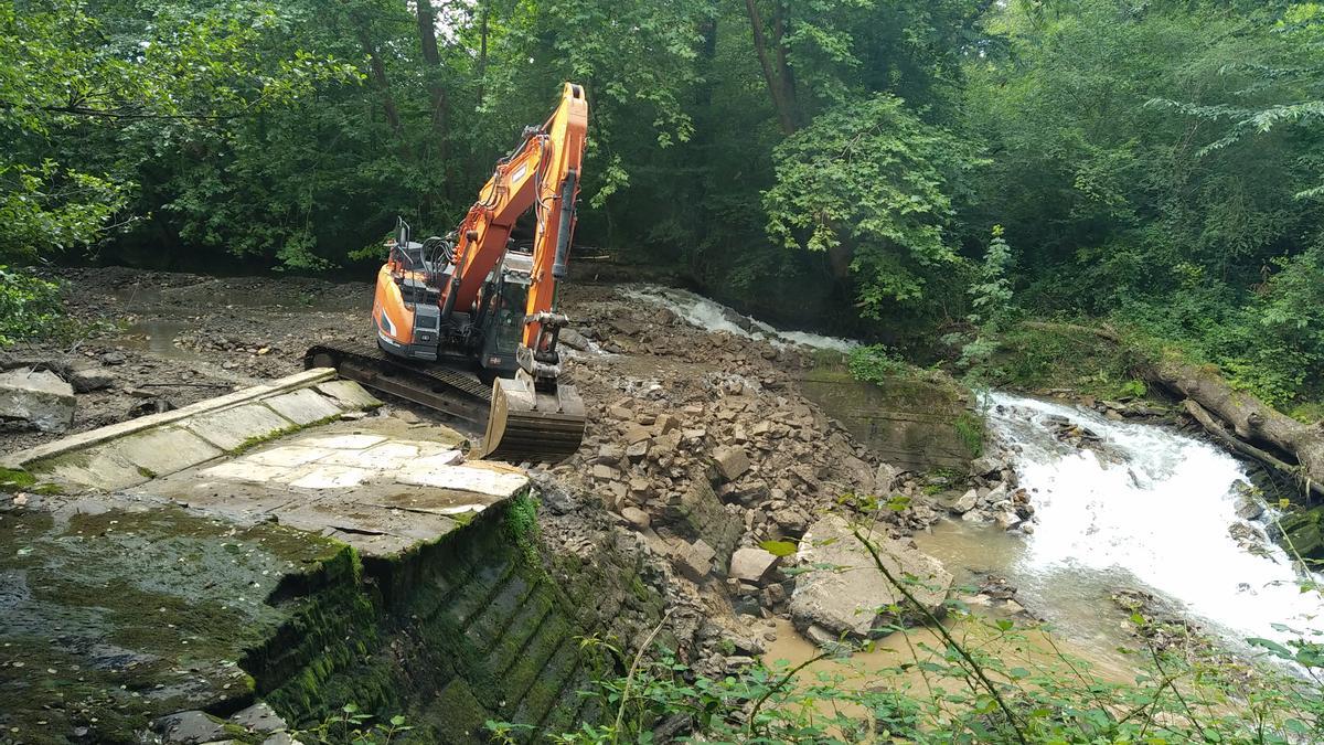 Una excavadora destruye una presa en un río.