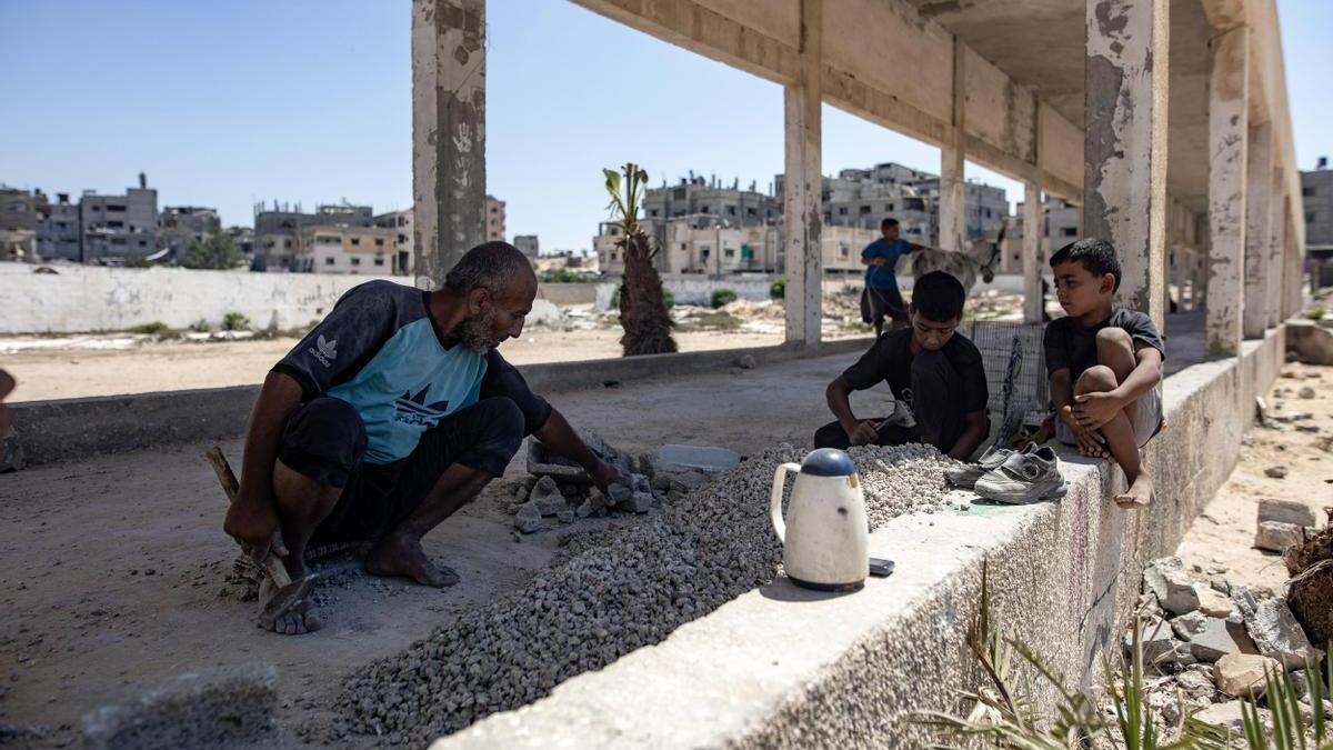 Maysara Omar y sus hijos, palestinos desplazados, rompen piedras que han recogido de las casas destruidas por ataques aéreos israelíes para venderlas y hacer lápidas, en Jan Yunis, el 21 de agosto de 2024.