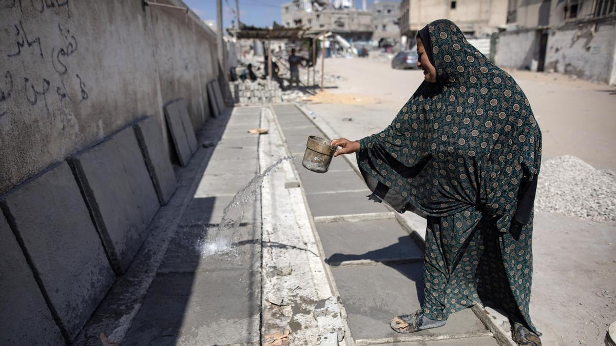 Hayat Abu Hatab, palestina desplazada, rocía agua sobre las lápidas que construyó con piedras recogidas de casas destruidas por ataques aéreos israelíes, en Jan Yunis 21 de agosto de 2024.