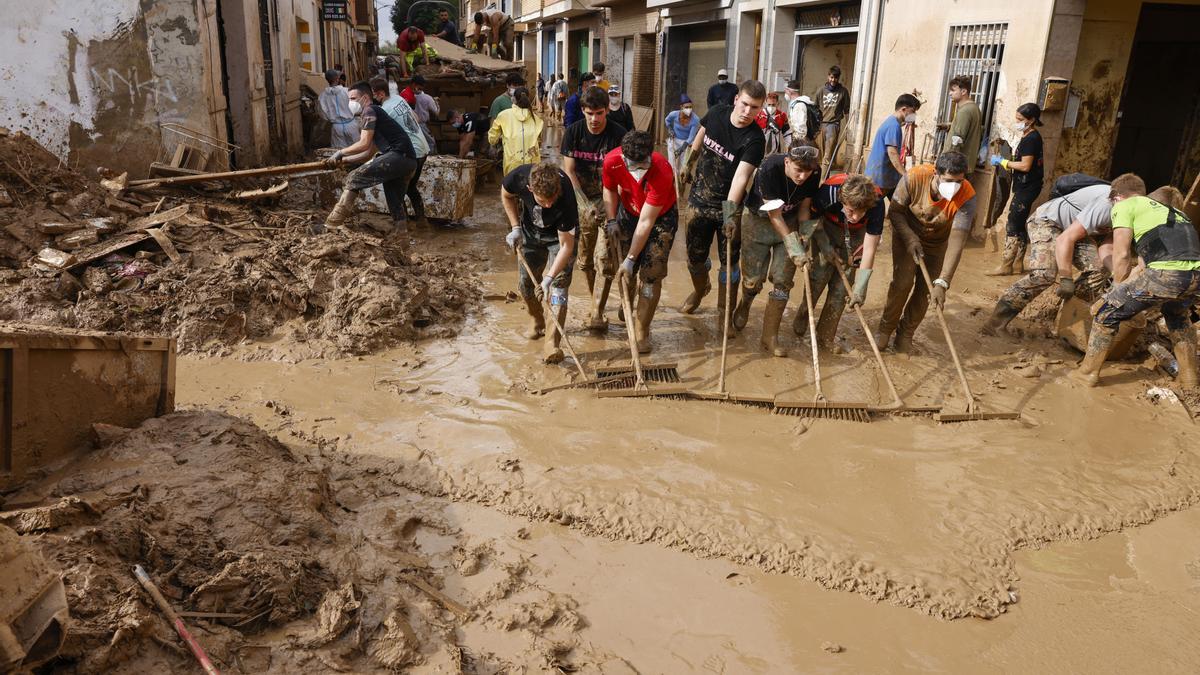 Voluntarios barren el lodo de una calle de Massanassa, cerca de casa de Cristina Durán