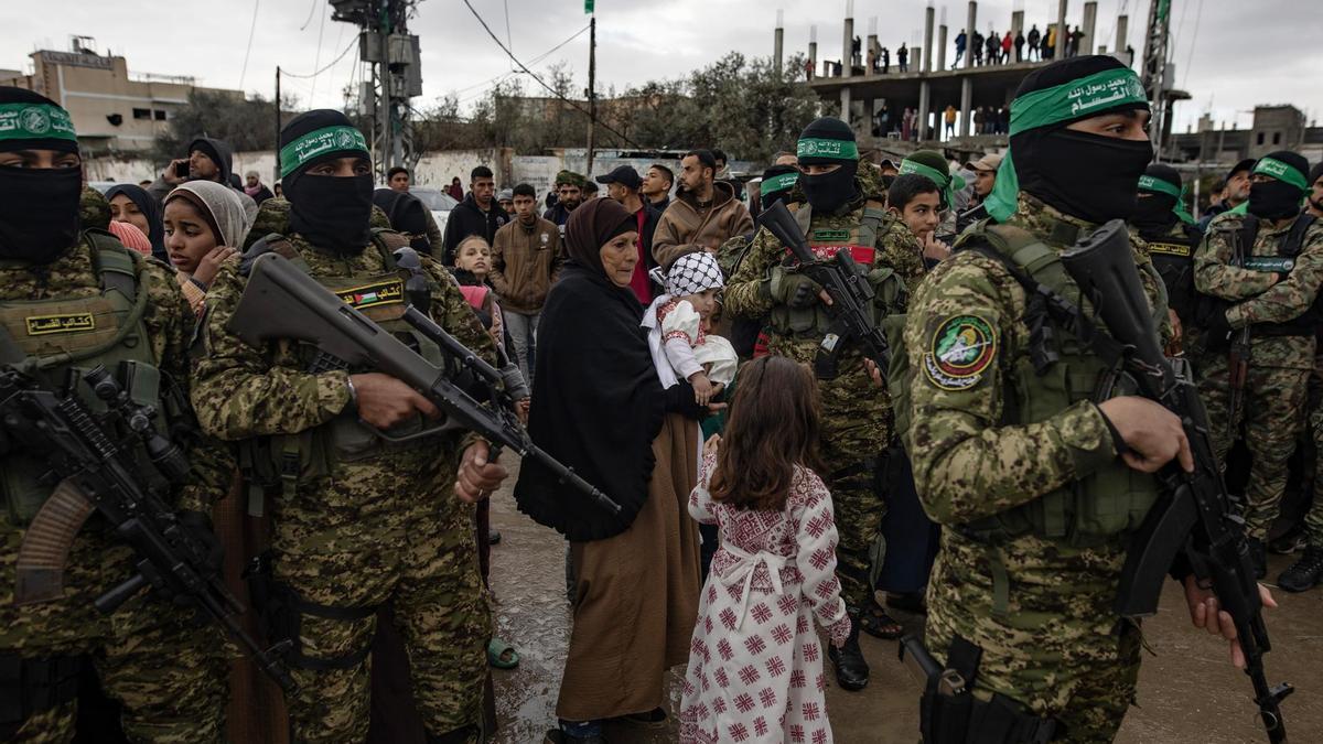 Un grupo de palestinos junto al cordón de seguridad establecido por milicianos de Hamás durante la liberación de rehenes en Rafá.