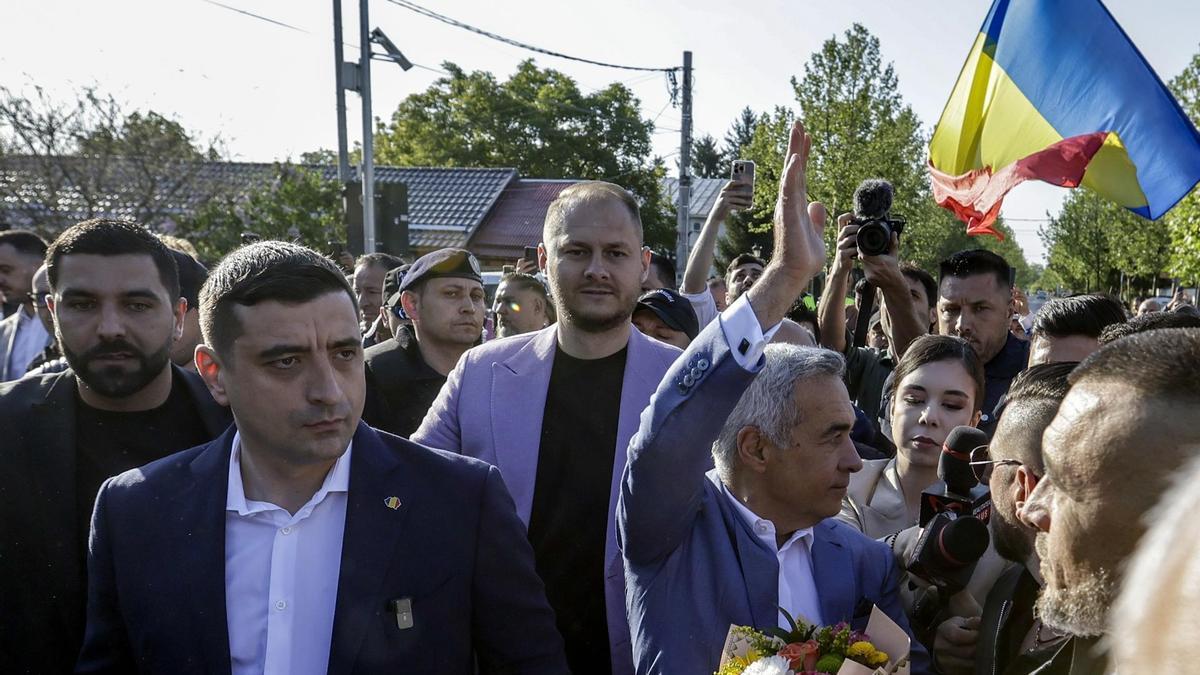 El candidato ultranacionalista George Simion acude a votar este domingo junto al antiguo candidato, inhabilitado, de su formación Calin Georgescu, que saluda a los presentes.