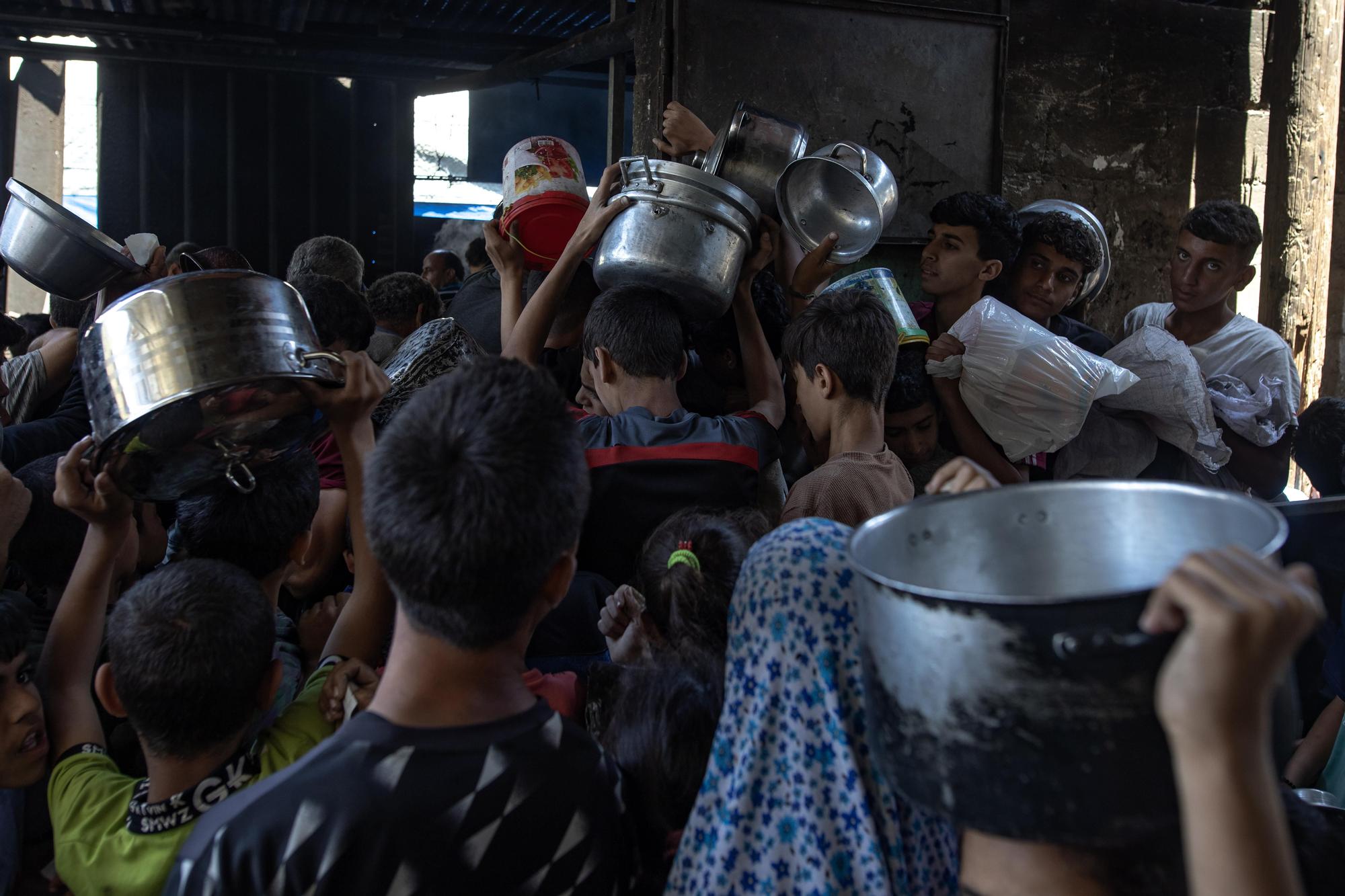 Cientos de palestinos desplazados se reúnen a las afueras del comedor benéfico Sokar en la ciudad de Gaza para recibir raciones limitadas de alimentos